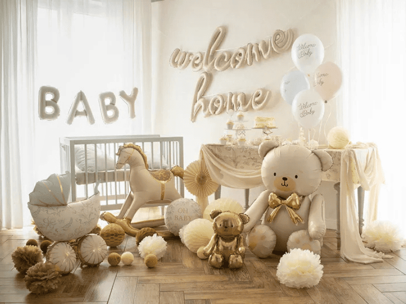 Allestimento festa nascita neutro oro e beige con palloncini Welcome Home e Baby, orsetti in foil, carrozzina decorativa, cavallino a dondolo e tavolo sweet table coordinato.