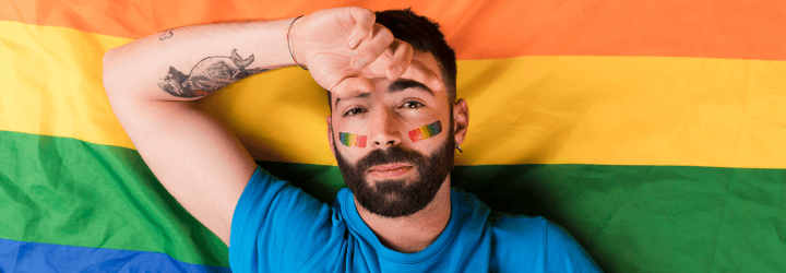 ragazzo con le guance dipinte con i colori del pride con lo sfondo una bandieta lgbtqia+