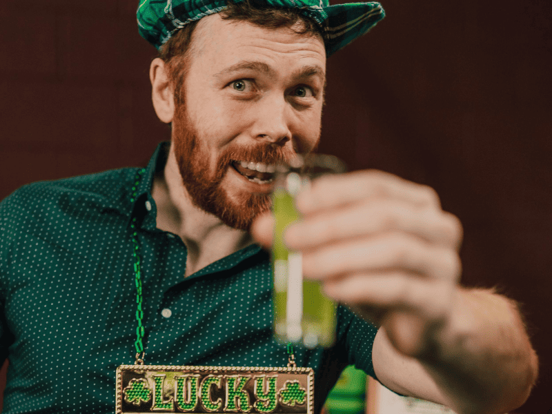 Uomo con cappello verde e collana Lucky brinda con drink verde per Festa di San Patrizio a tema Irlanda